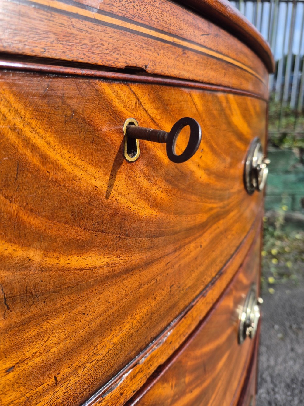 A Regency period bowfront chest of drawers crafted from flame mahogany veneer with three drawers and brass oval handles. View IX
