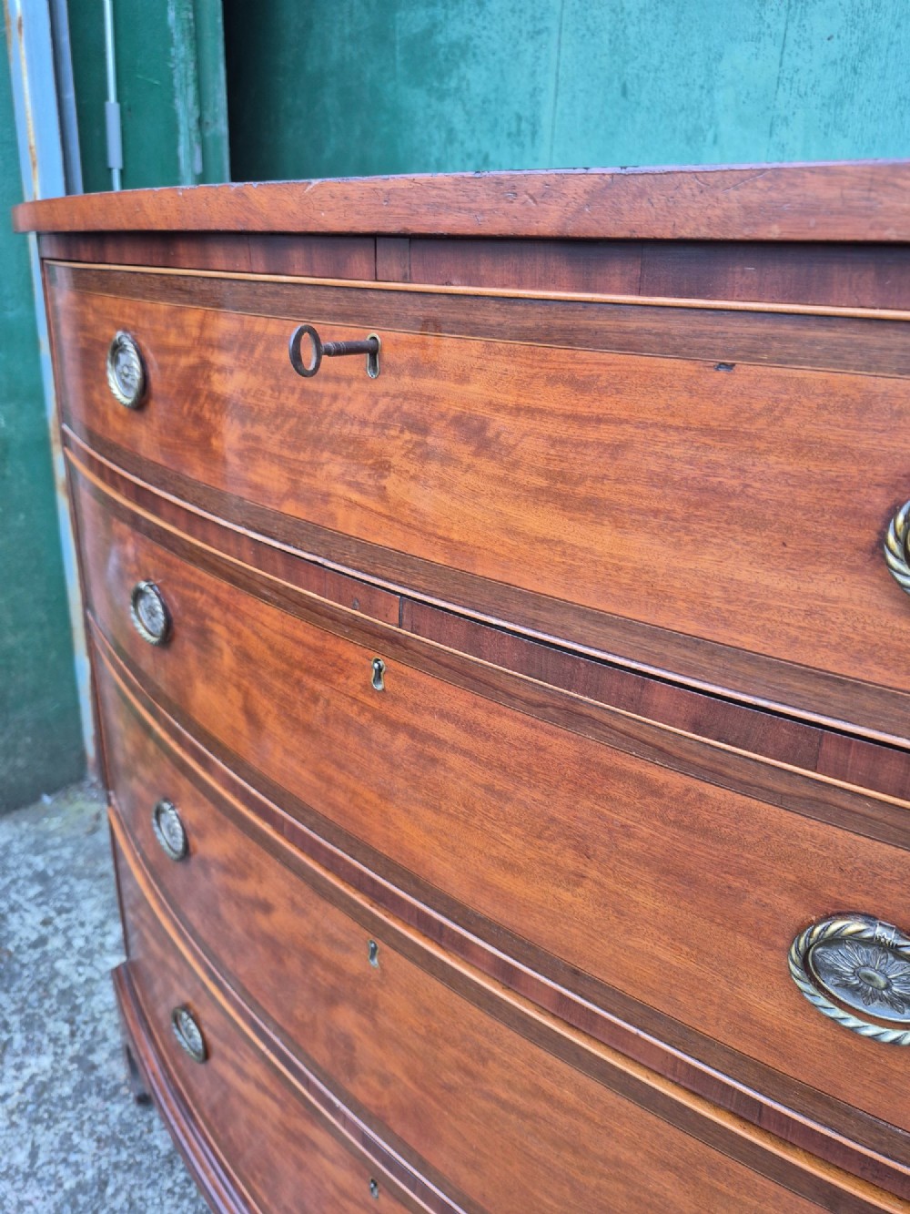 A Regency period satinwood bowfront chest of drawers featuring four graduated drawers with oval brass handles and bracket feet. View III