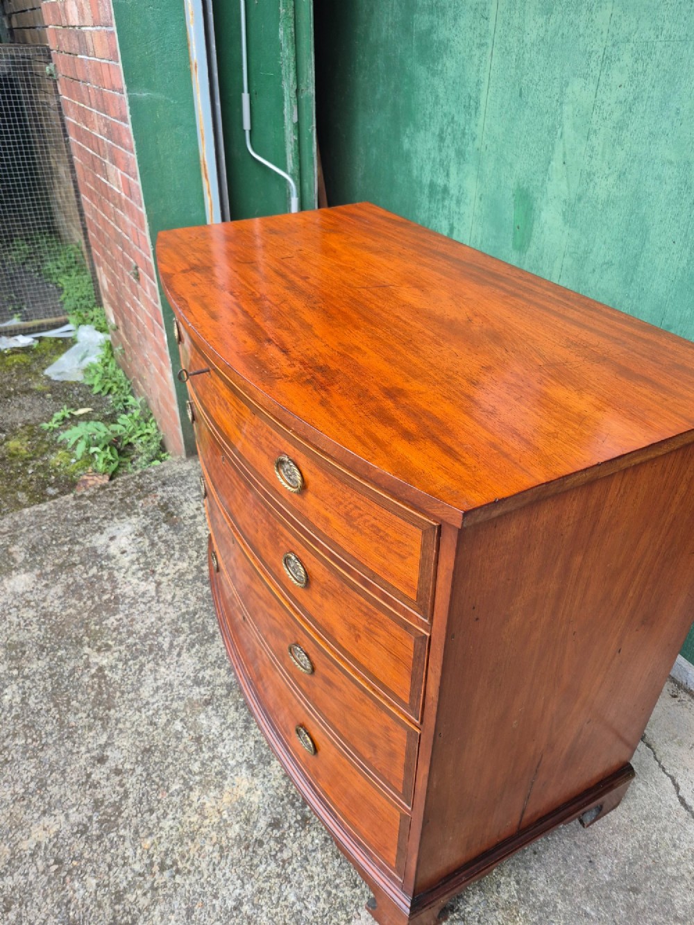 A Regency period satinwood bowfront chest of drawers featuring four graduated drawers with oval brass handles and bracket feet. View IV