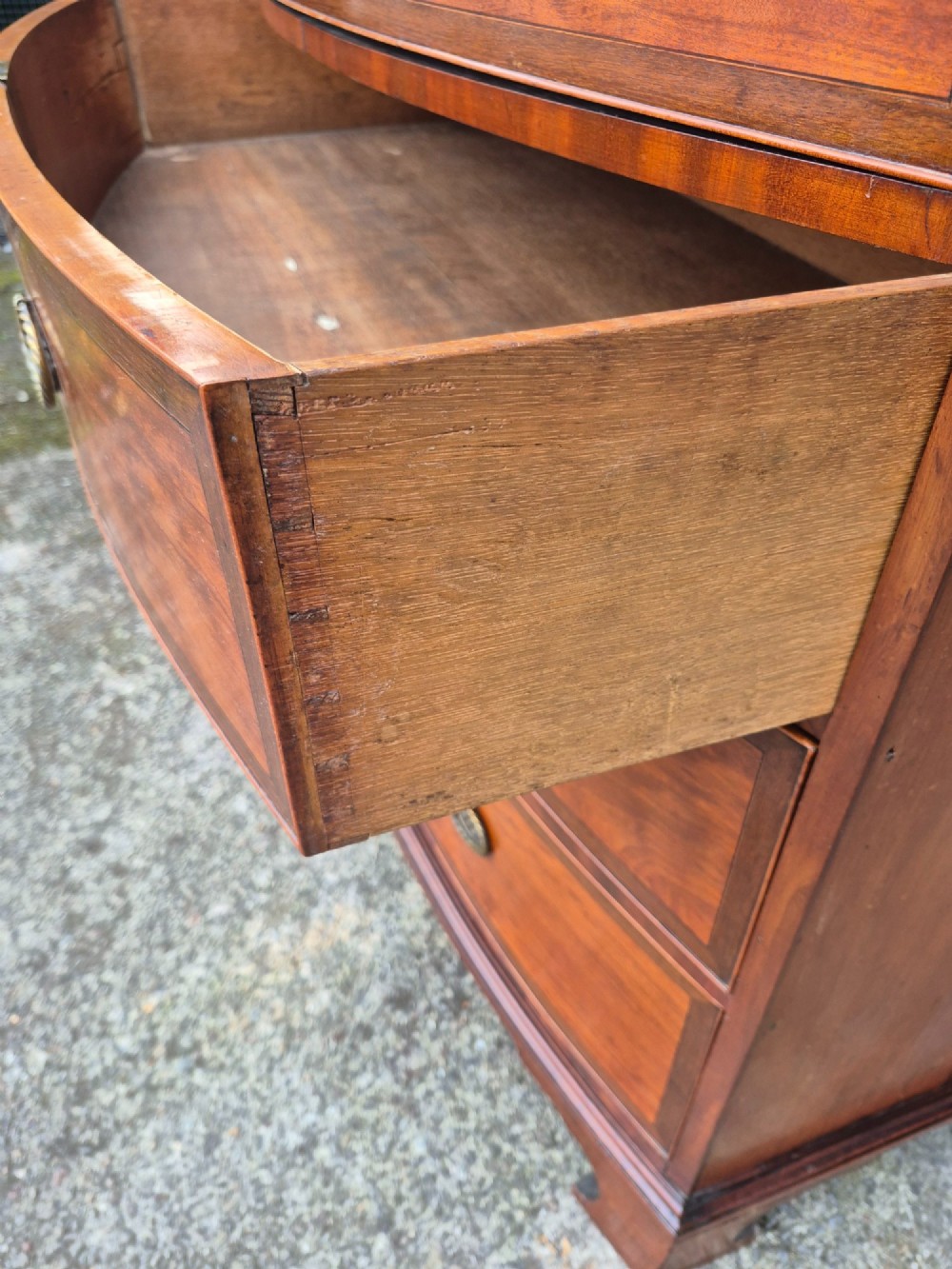 A Regency period satinwood bowfront chest of drawers featuring four graduated drawers with oval brass handles and bracket feet. View VII