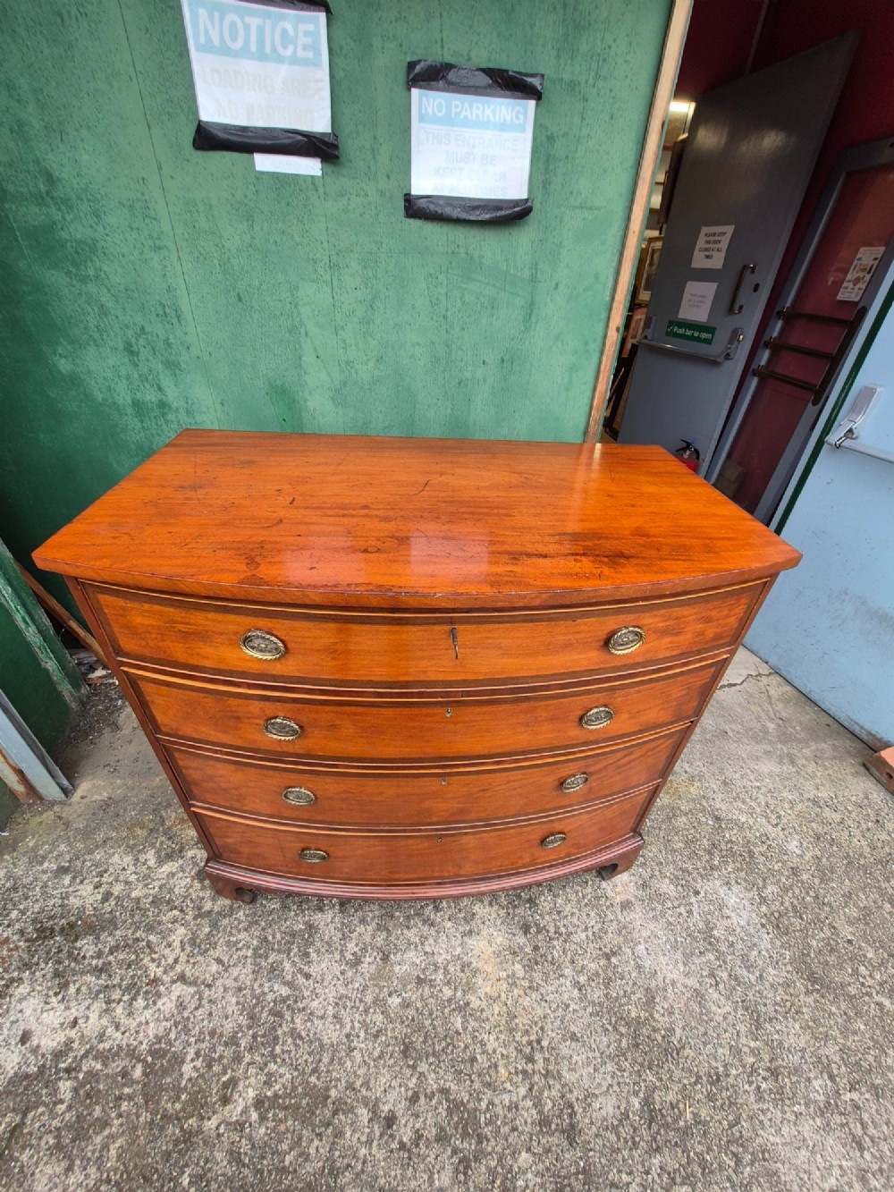 A Regency period satinwood bowfront chest of drawers featuring four graduated drawers with oval brass handles and bracket feet. View IX