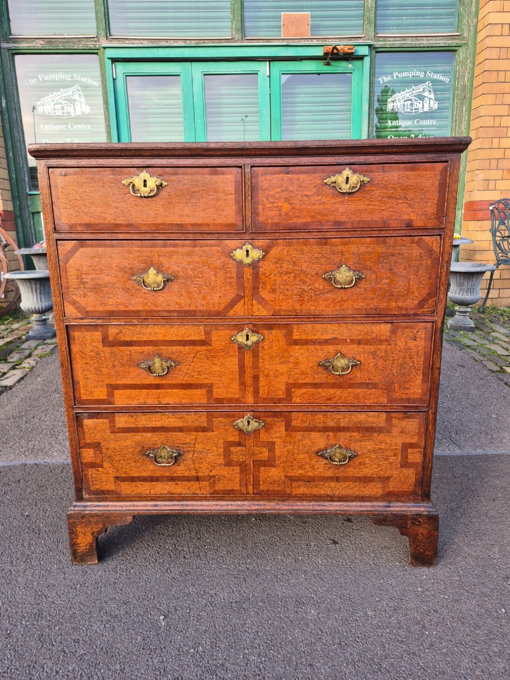 An Early Georgian oak and walnut chest of drawers featuring geometric wood banding, engraved brass handles, and bracket feet.