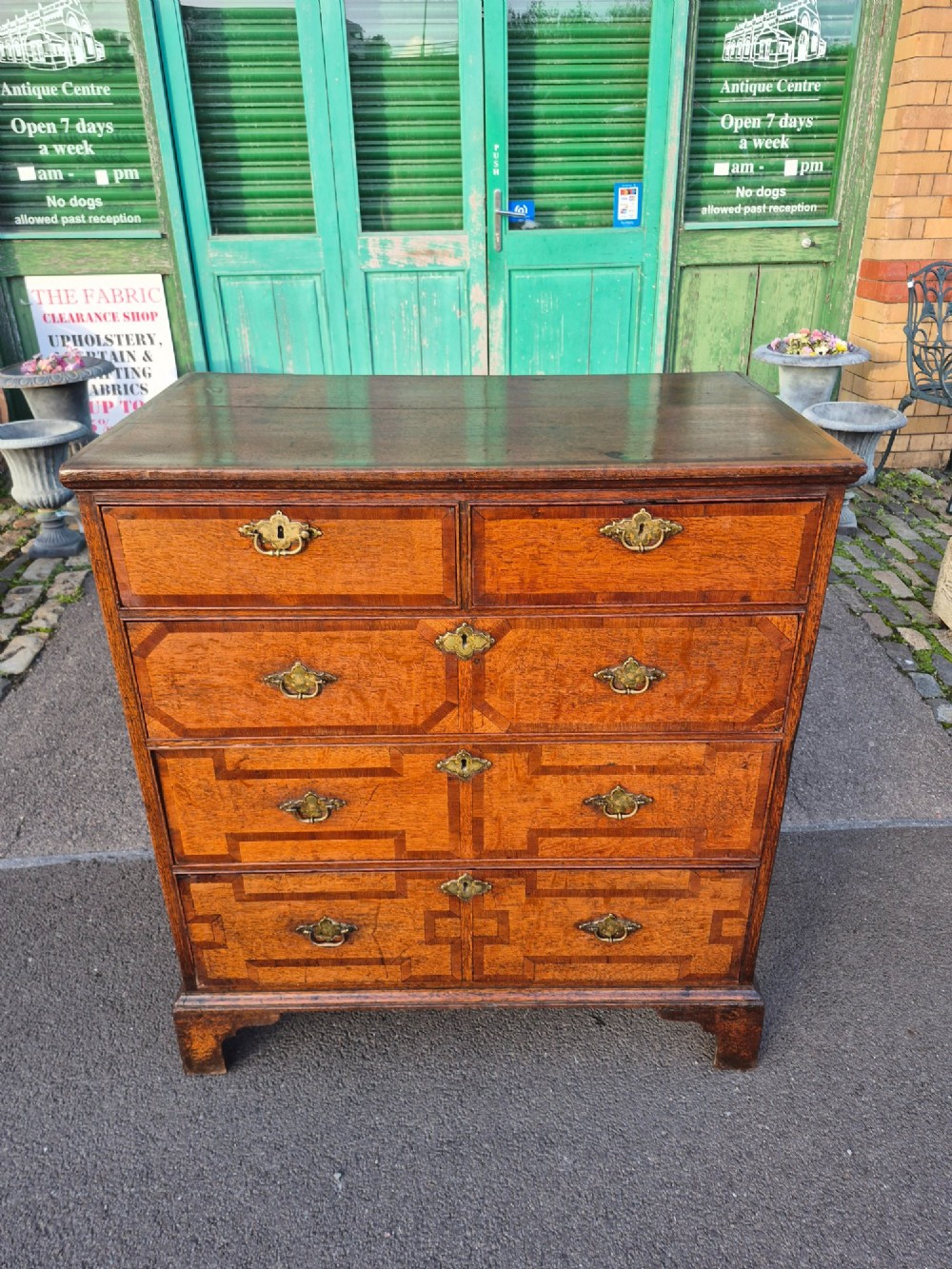 An Early Georgian oak and walnut chest of drawers featuring geometric wood banding, engraved brass handles, and bracket feet. View II