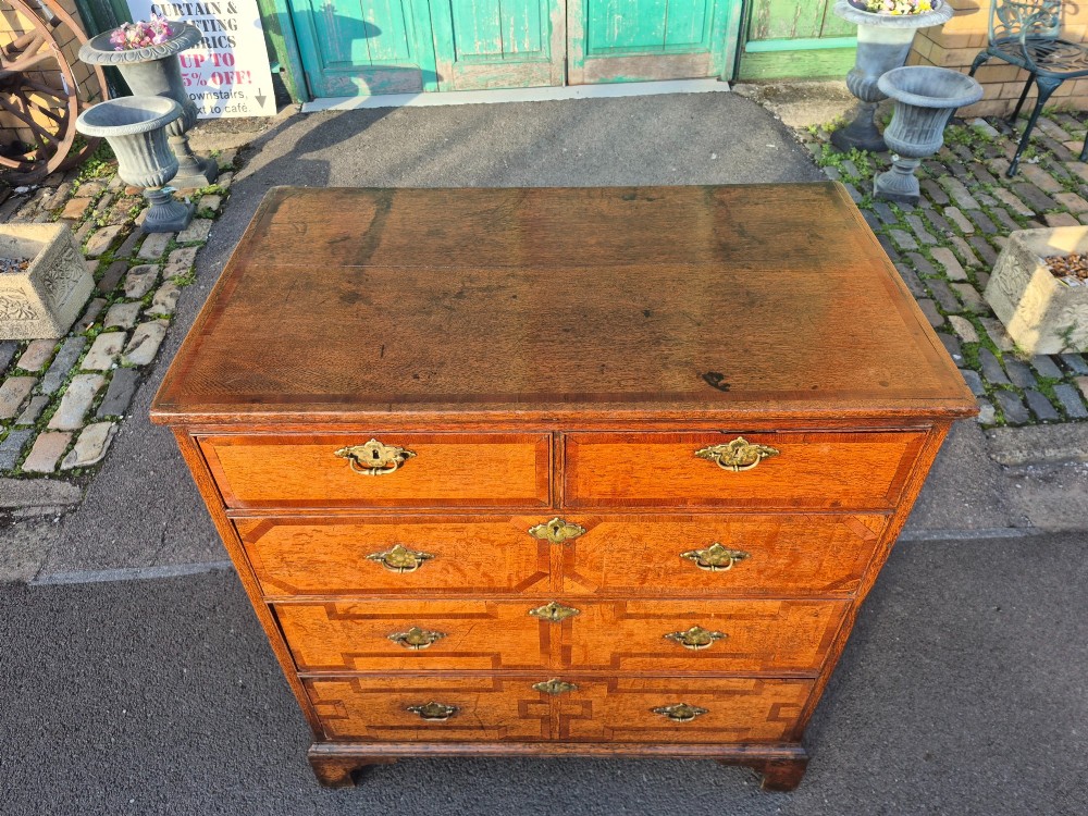 An Early Georgian oak and walnut chest of drawers featuring geometric wood banding, engraved brass handles, and bracket feet. View VI