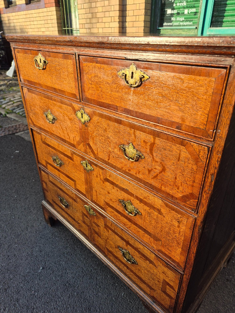 An Early Georgian oak and walnut chest of drawers featuring geometric wood banding, engraved brass handles, and bracket feet. View VIII