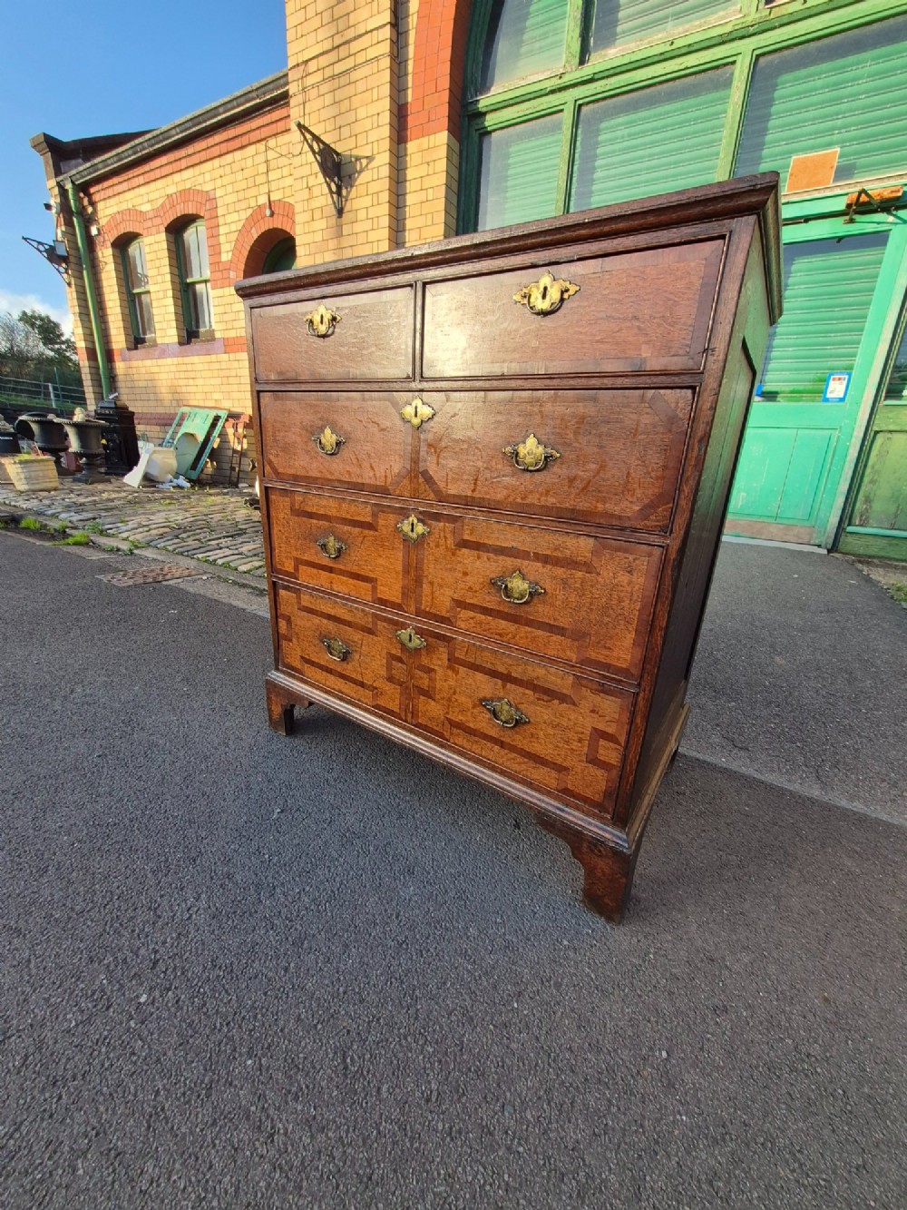 An Early Georgian oak and walnut chest of drawers featuring geometric wood banding, engraved brass handles, and bracket feet. View XII