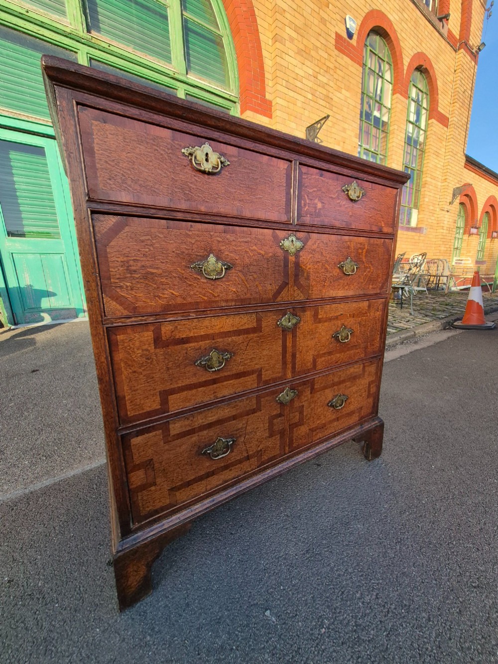An Early Georgian oak and walnut chest of drawers featuring geometric wood banding, engraved brass handles, and bracket feet. View XIII