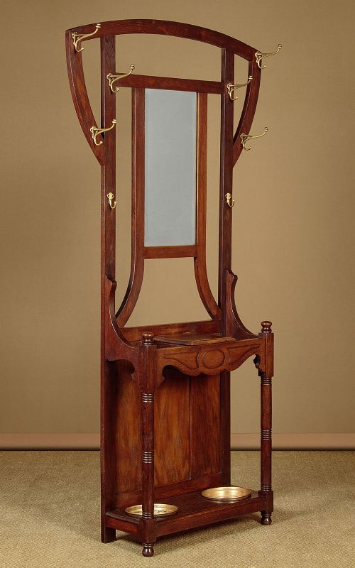 An Art Nouveau oak hallstand featuring an arched upper frame, brass coat hooks, central mirror, glove box, and bottom umbrella stand with two brass drip trays. View II