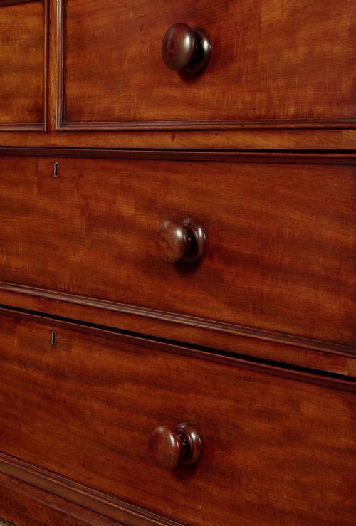 A nineteenth-century mahogany linen press featuring flame mahogany panel doors opening to reveal timber trays above a base of four drawers with turned wooden knobs. View XI