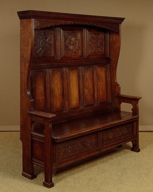A dark oak canopy box settle featuring intricate carved floral panels, a tall fielded-panel back, and a lift-up storage seat base. View II