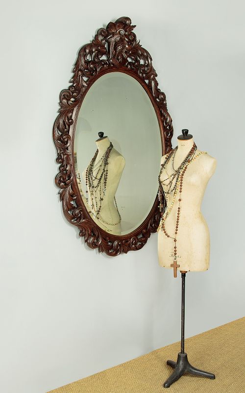 A late Victorian oval wall mirror featuring a carved dark oak frame with acanthus scrollwork and a crest motif enclosing a bevelled glass mirror plate. View II