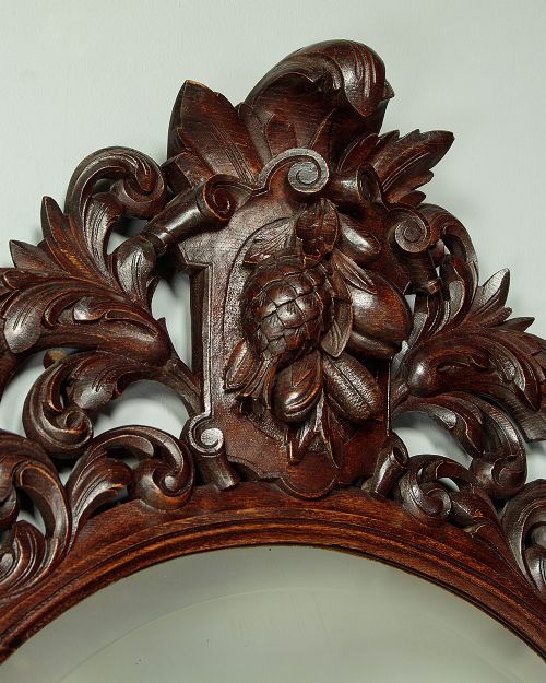 A late Victorian oval wall mirror featuring a carved dark oak frame with acanthus scrollwork and a crest motif enclosing a bevelled glass mirror plate. View IV
