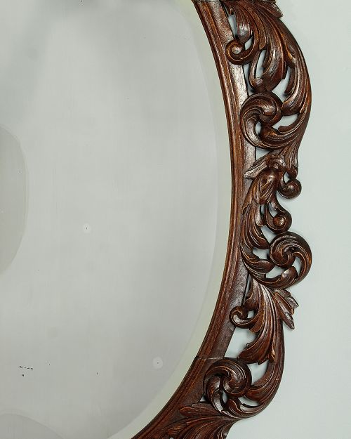 A late Victorian oval wall mirror featuring a carved dark oak frame with acanthus scrollwork and a crest motif enclosing a bevelled glass mirror plate. View VI