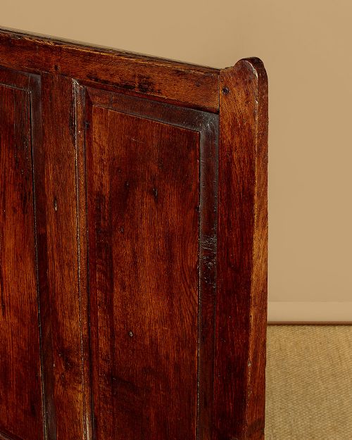 A dark oak 18th-century high-back box settle featuring fielded panels, shaped open armrests, and a hinged lid seat. View V