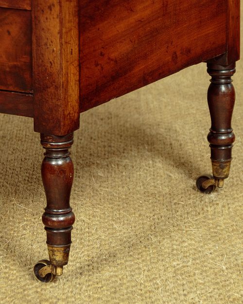 A dark mahogany Canterbury featuring four open slatted dividers above a single drawer with turned legs and brass castors. View VII
