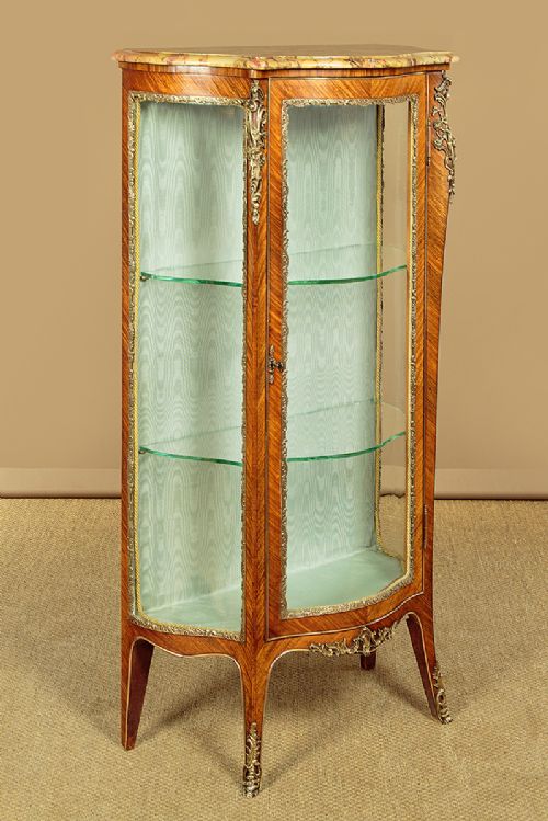 A small French Louis XV style vitrine with curved glass sides, a single glazed door, gilded brass mounts, a marble top, and a pale green fabric-lined interior with glass shelves. View II