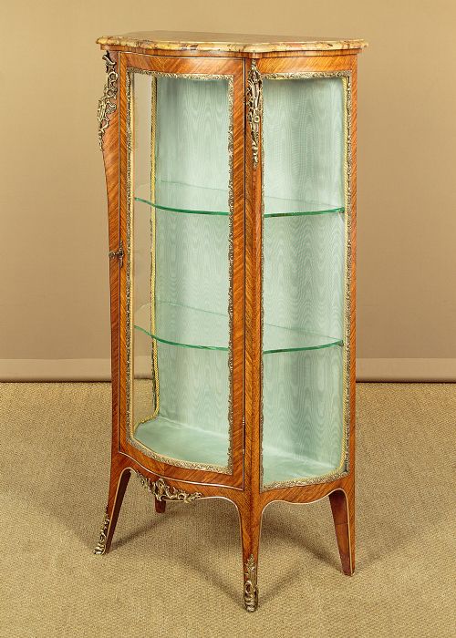 A small French Louis XV style vitrine with curved glass sides, a single glazed door, gilded brass mounts, a marble top, and a pale green fabric-lined interior with glass shelves. View III
