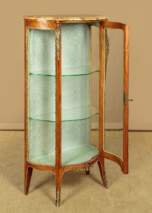 A small French Louis XV style vitrine with curved glass sides, a single glazed door, gilded brass mounts, a marble top, and a pale green fabric-lined interior with glass shelves. View IV