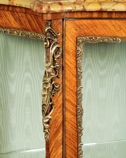 A small French Louis XV style vitrine with curved glass sides, a single glazed door, gilded brass mounts, a marble top, and a pale green fabric-lined interior with glass shelves. View VII