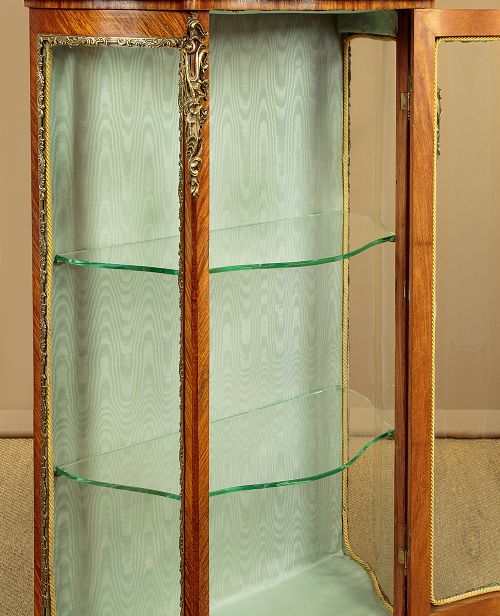 A small French Louis XV style vitrine with curved glass sides, a single glazed door, gilded brass mounts, a marble top, and a pale green fabric-lined interior with glass shelves. View VIII