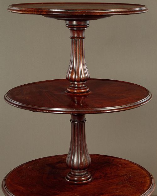 A mahogany three-tier dumb waiter featuring graduated circular trays supported by fluted central columns on a tripod base with brass castors. View V