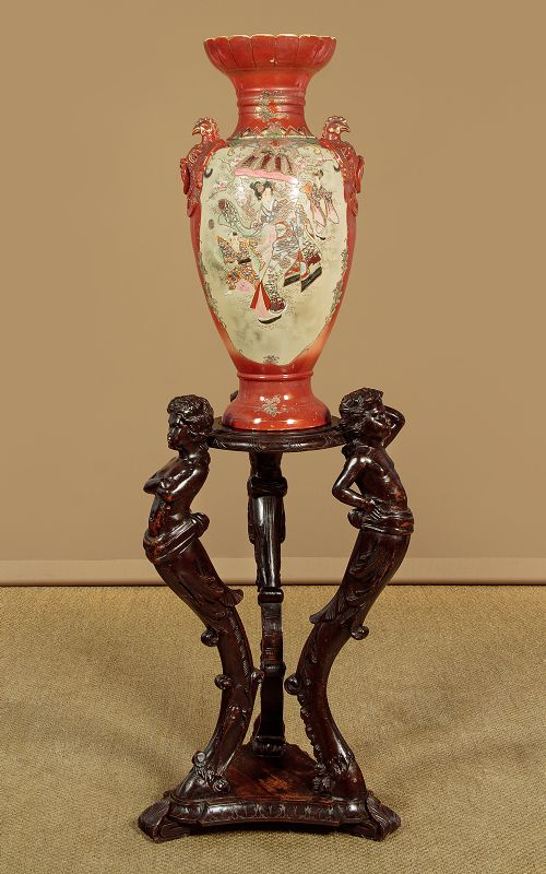 A dark carved wooden pedestal stand featuring three figurative sculpted supports on a tripartite base supporting a circular carved top. View III