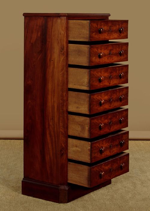 A tall and narrow Victorian mahogany bank of seven graduated drawers featuring flame mahogany veneer fronts, turned wood knob handles, and a solid plinth base. View IV