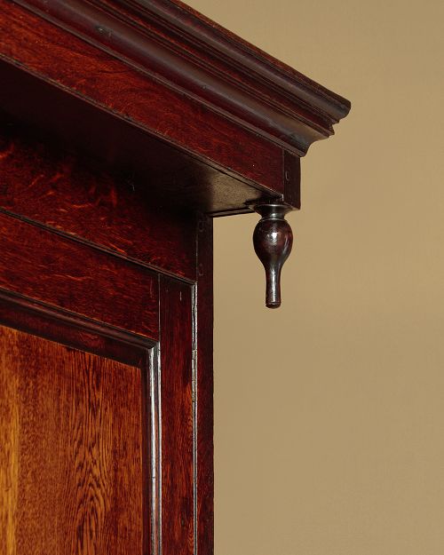 An 18th-century dark Welsh oak cwpwrdd deuddarn featuring an overhanging canopy with drop pendants, upper fielded panel doors, two drawers, and lower cupboard doors. View VI