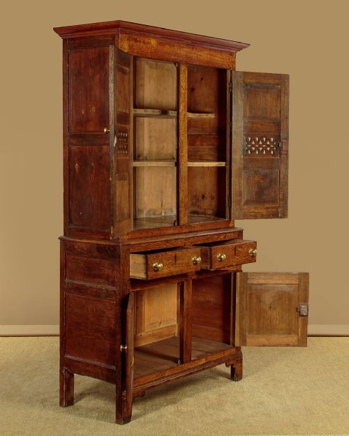A two-part antique warm brown oak bread and cheese cupboard featuring upper doors with lattice ventilation fretwork over lower drawers and panelled cupboard doors. View IV