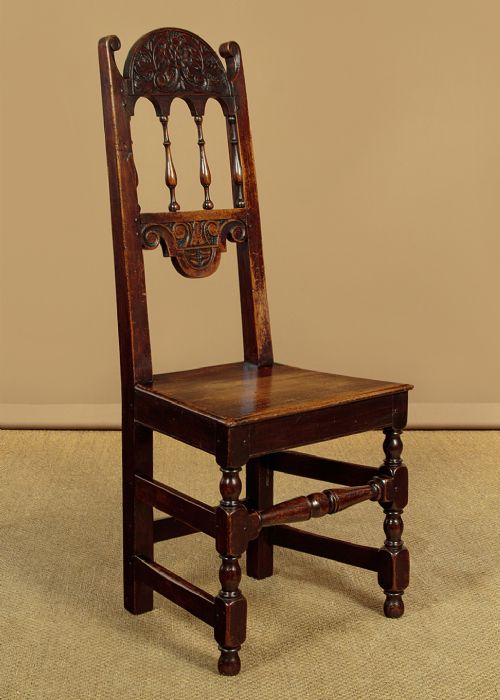 A set of four dark oak dining chairs featuring carved crest rails, arcaded spindle backs, wooden seats, and turned front legs. View II