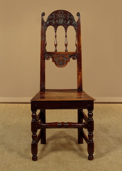 A set of four dark oak dining chairs featuring carved crest rails, arcaded spindle backs, wooden seats, and turned front legs. View III