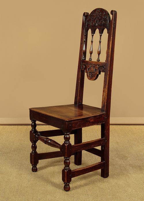 A set of four dark oak dining chairs featuring carved crest rails, arcaded spindle backs, wooden seats, and turned front legs. View IV