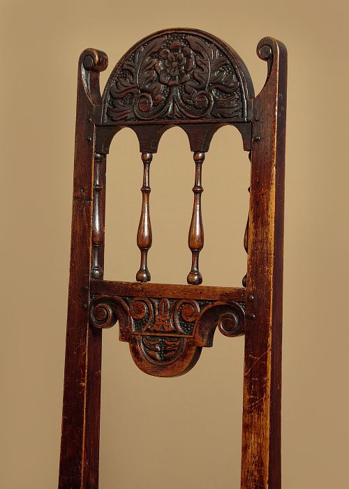 A set of four dark oak dining chairs featuring carved crest rails, arcaded spindle backs, wooden seats, and turned front legs. View V