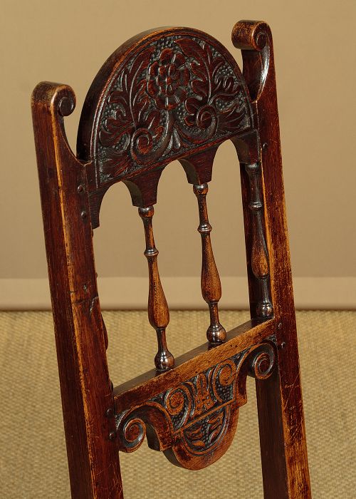 A set of four dark oak dining chairs featuring carved crest rails, arcaded spindle backs, wooden seats, and turned front legs. View VI