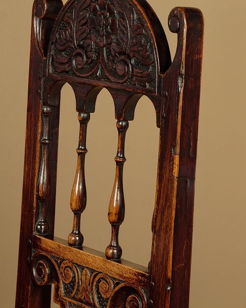 A set of four dark oak dining chairs featuring carved crest rails, arcaded spindle backs, wooden seats, and turned front legs. View VII