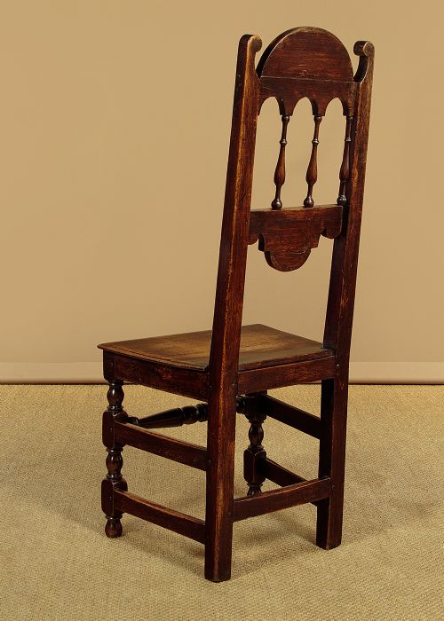 A set of four dark oak dining chairs featuring carved crest rails, arcaded spindle backs, wooden seats, and turned front legs. View XI