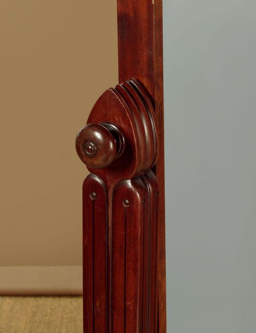 A 19th-century mahogany cheval mirror featuring a rectangular swivelling glass frame set between carved reeded uprights on scroll feet. View VI
