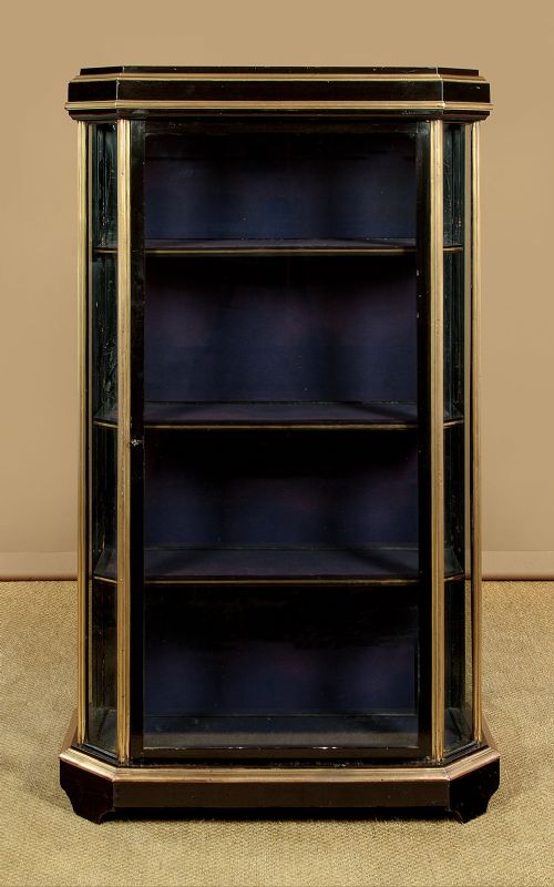 An Art Deco ebonised tall display cabinet featuring brass mounts, glazed side panels, a single glass door, and fabric-lined interior shelving. View II