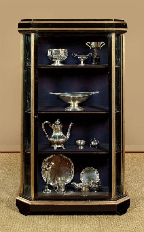 An Art Deco ebonised tall display cabinet featuring brass mounts, glazed side panels, a single glass door, and fabric-lined interior shelving. View III