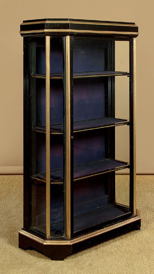 An Art Deco ebonised tall display cabinet featuring brass mounts, glazed side panels, a single glass door, and fabric-lined interior shelving. View IV