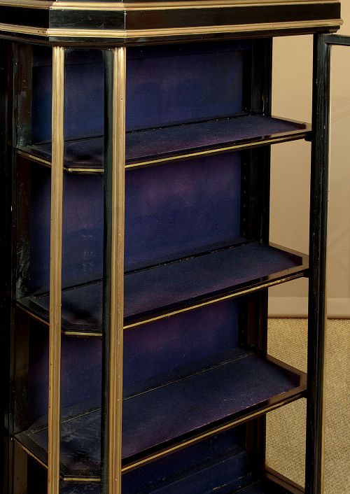 An Art Deco ebonised tall display cabinet featuring brass mounts, glazed side panels, a single glass door, and fabric-lined interior shelving. View VIII