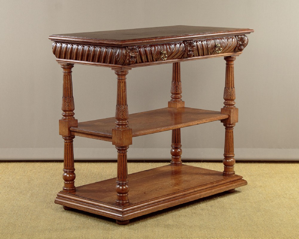 A late Victorian carved oak dumb waiter featuring two lower shelves supported by fluted columns and a frieze decorated with carved gadrooning and lion masks.