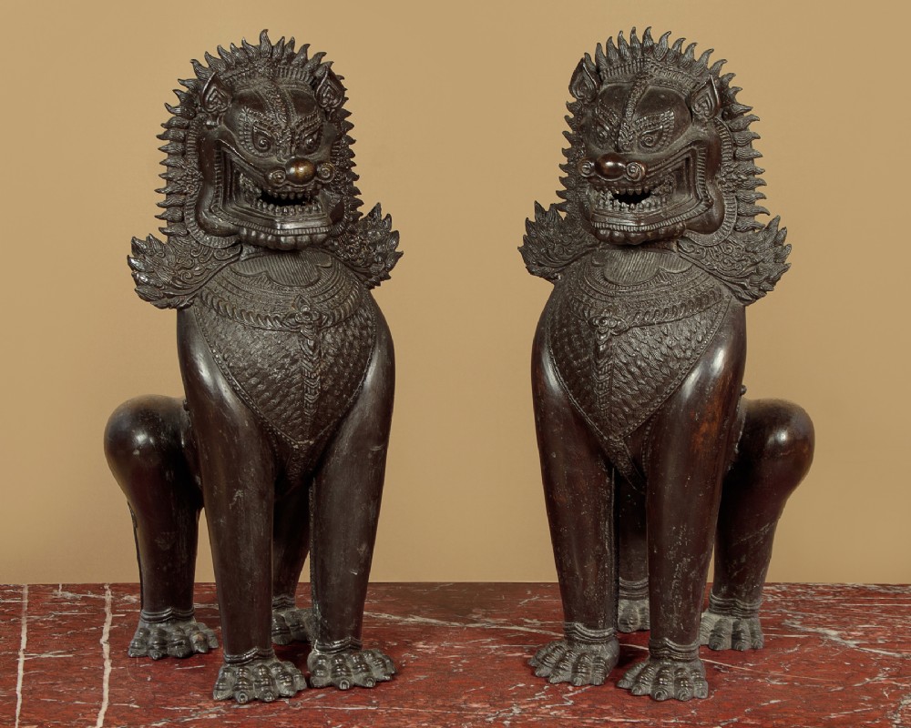 A pair of upright cast dark bronze temple lion sculptures featuring stylised manes and detailed chest ornamentation.