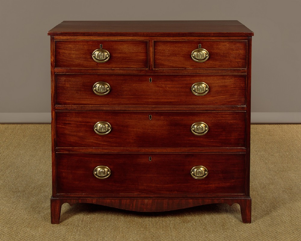 A George III mahogany chest of drawers featuring two short over three long graduated drawers with oval brass handles on shaped bracket feet.