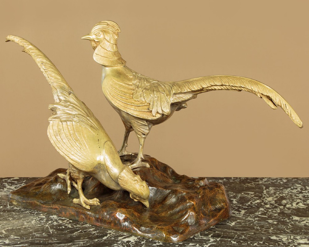 An Art Deco gilt metal sculpture depicting two golden pheasants standing on a textured dark brown base.
