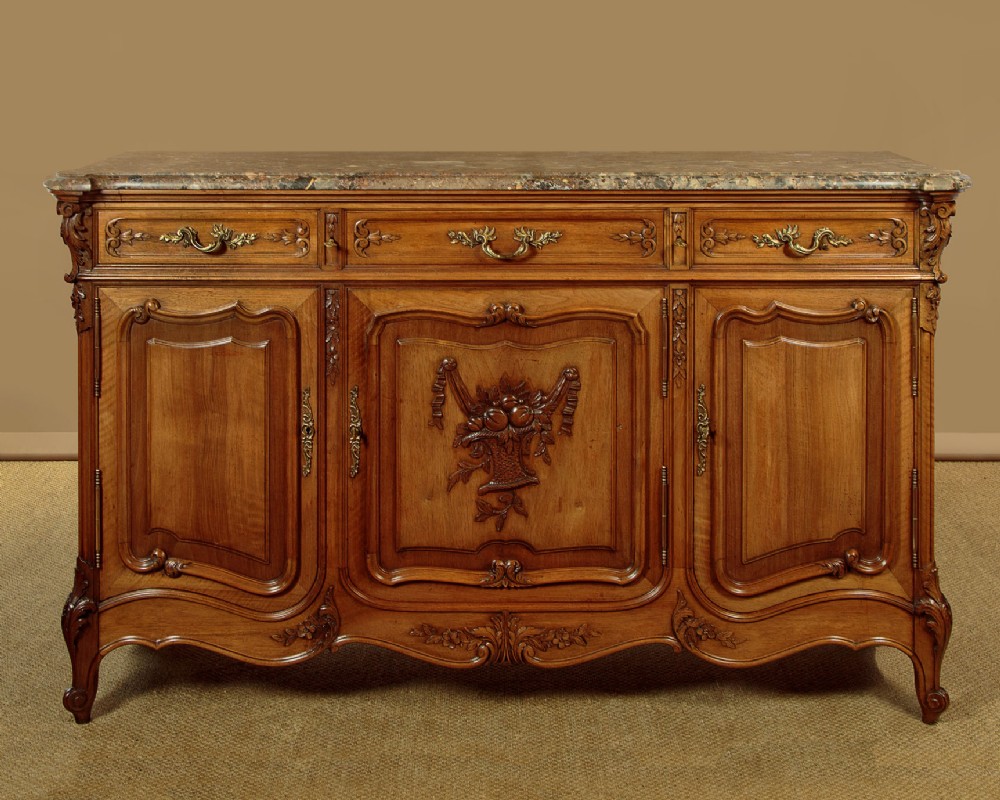 A carved French wooden sideboard featuring three panelled cupboard doors, brass handles, a central fruit motif carving, and a polished marble top.