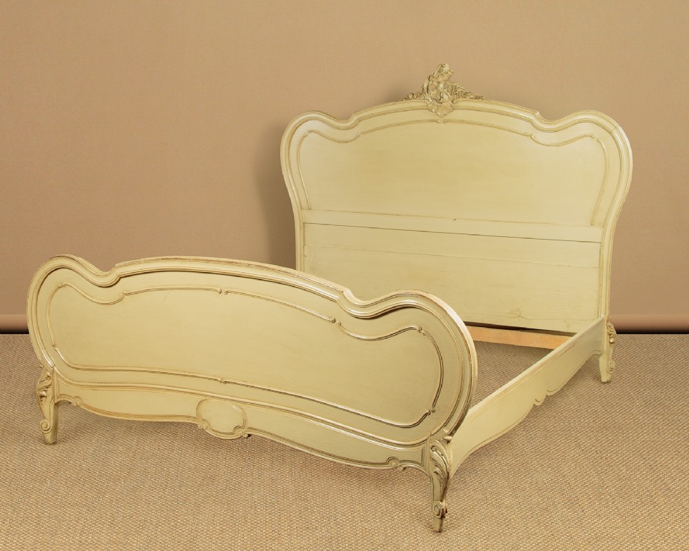 A French double bed frame painted in off-white cream with carved Rococo cresting on the headboard and serpentine moulding.