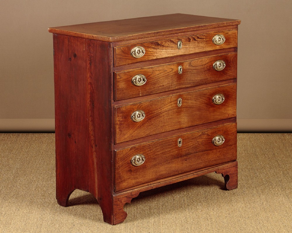 A small Georgian elm chest of four graduated drawers featuring brass oval handles, keyholes, and bracket feet.