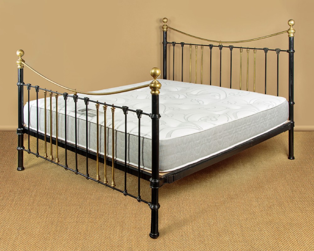 Late Victorian king-size bedstead featuring a black painted iron frame, vertical spindles, brass accents, and dipped brass top rails with brass ball finials.