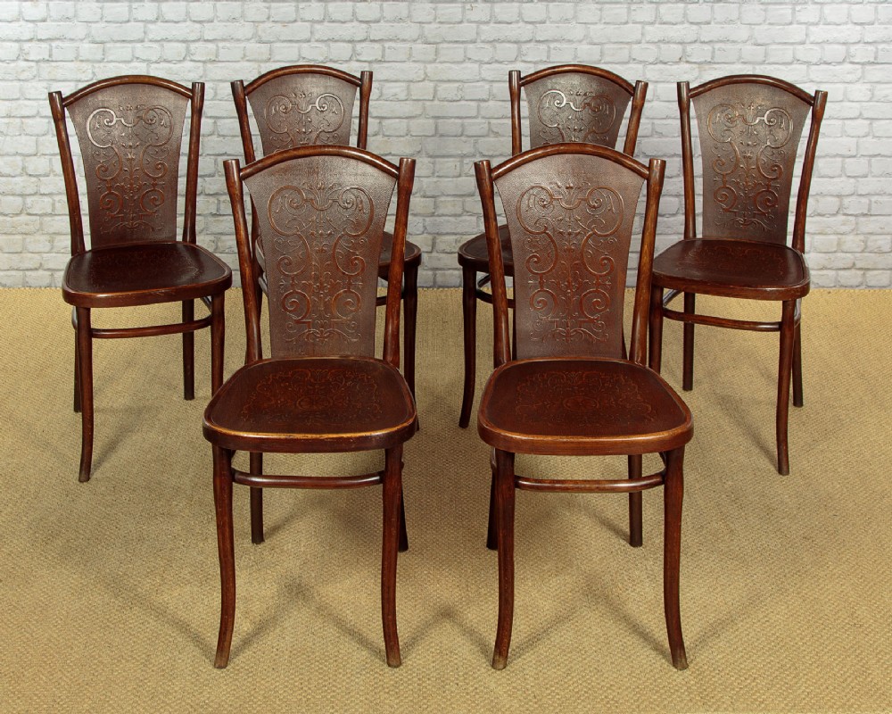 A set of six dark brown bentwood dining chairs with embossed scrollwork backrests and seats.